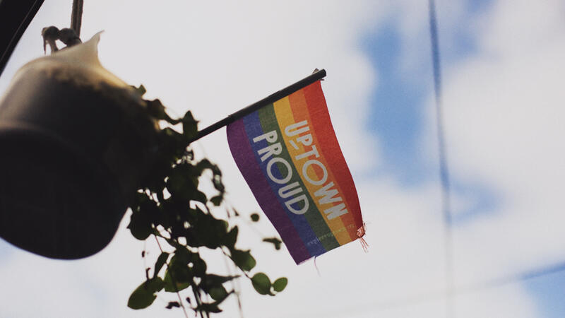 Small rainbow flag flying against a blue sky that reads Uptown Proud